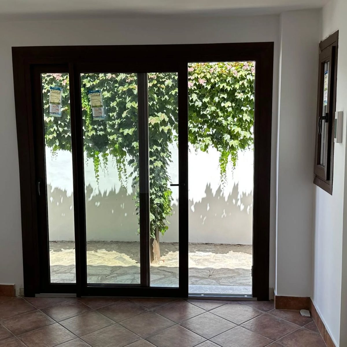Corredera de aluminio oscura con hojas fijas hacia un patio con hiedra